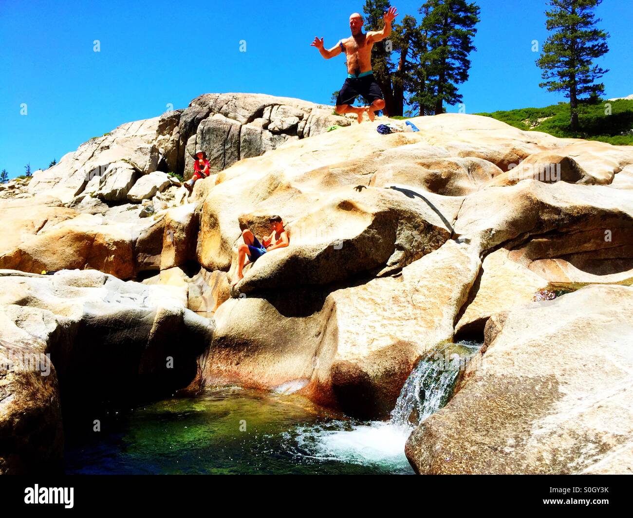 Summer adventures. Man jumps from high rock ledge into cool spring pool below. Stock Photo
