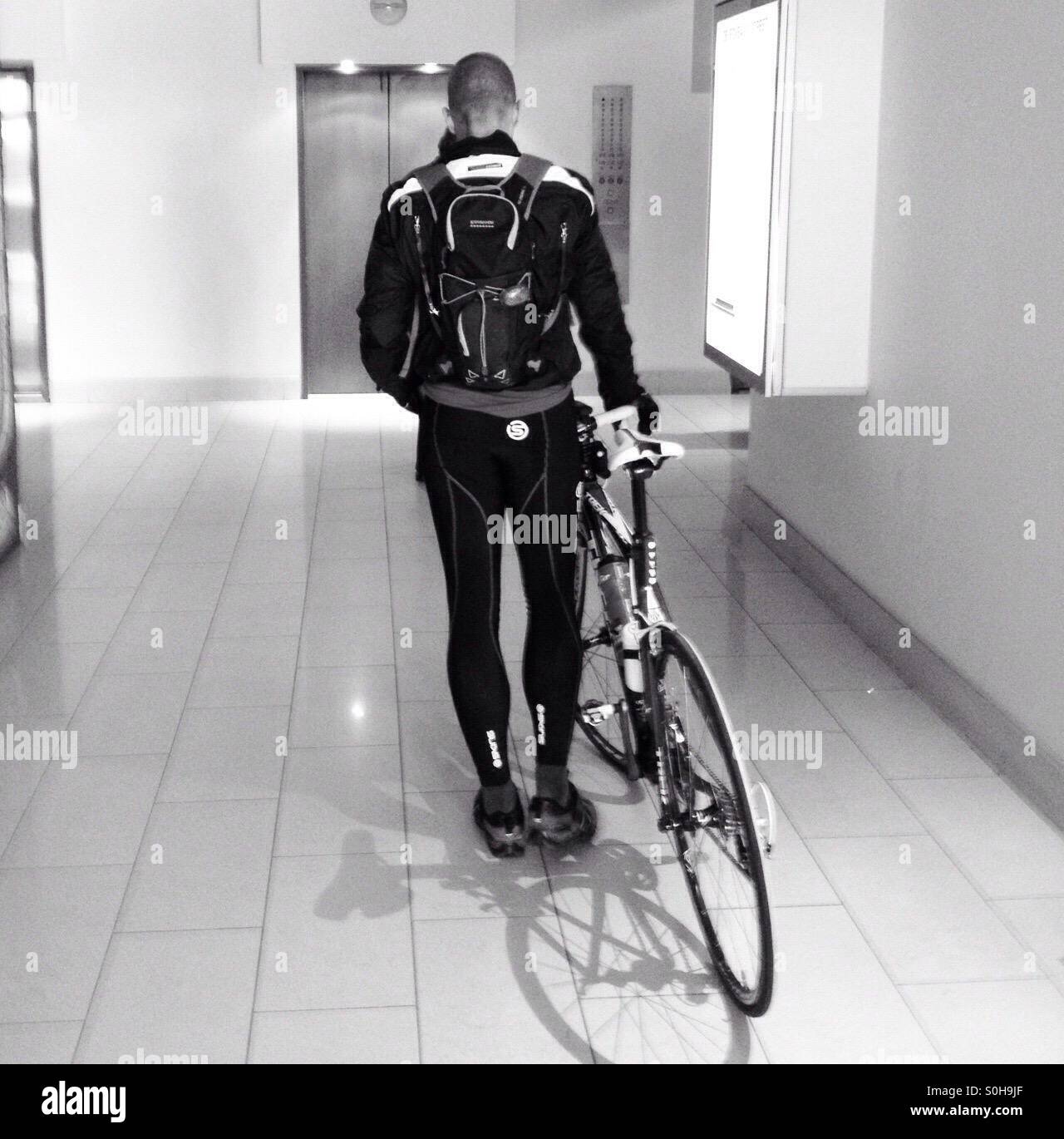 A cyclist arriving at work walking his bike in a lobby in an office building in Sydney, Australia - Smartphone Captured Stock Image