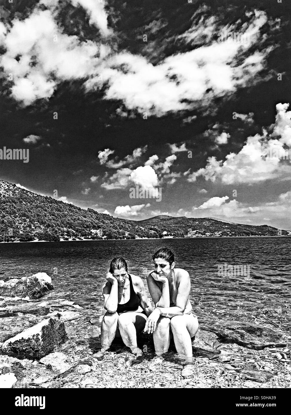 Mother and daughter chatting while sitting on a rock in the sea. - Smartphone Captured Stock Image