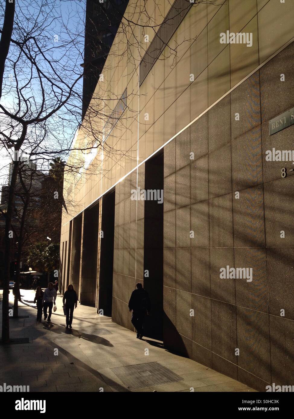 Silhouetted people walking near a tall building in Sydney Australia in winter time Stock Photo