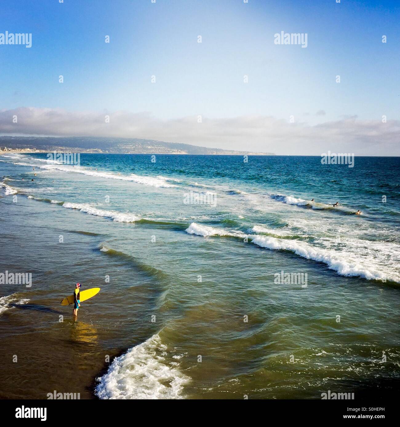 A surfer walks out to the surf. Manhattan Beach, California USA. Stock Photo