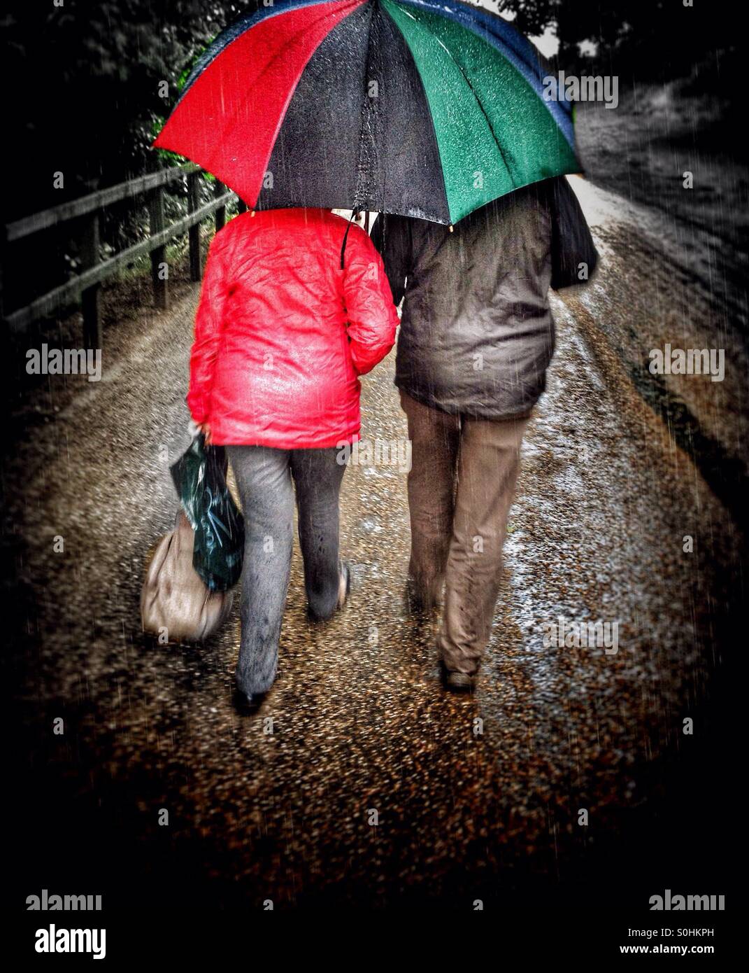 Elderly couple walking in rain under a large umbrella Stock Photo