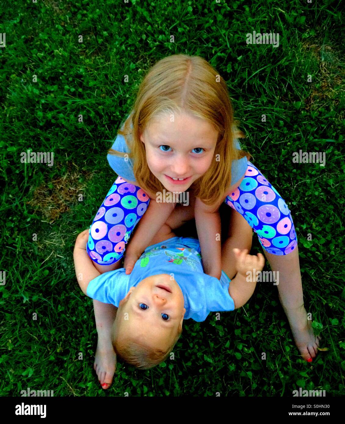 Siblings holding each other are sitting on a grass Stock Photo