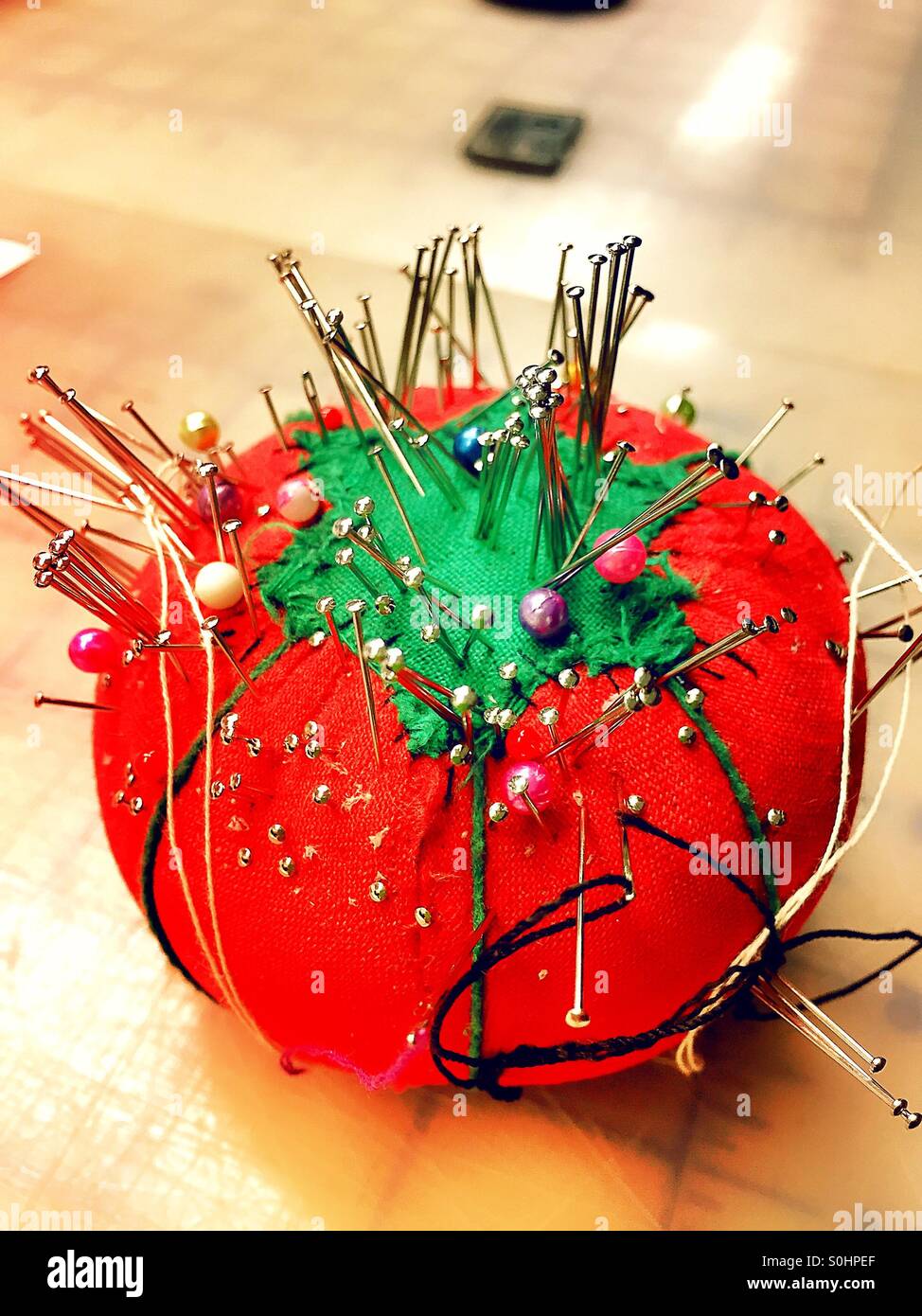 Pincushion in the shape of a red tomato is filled with pins. - Smartphone Captured Stock Image