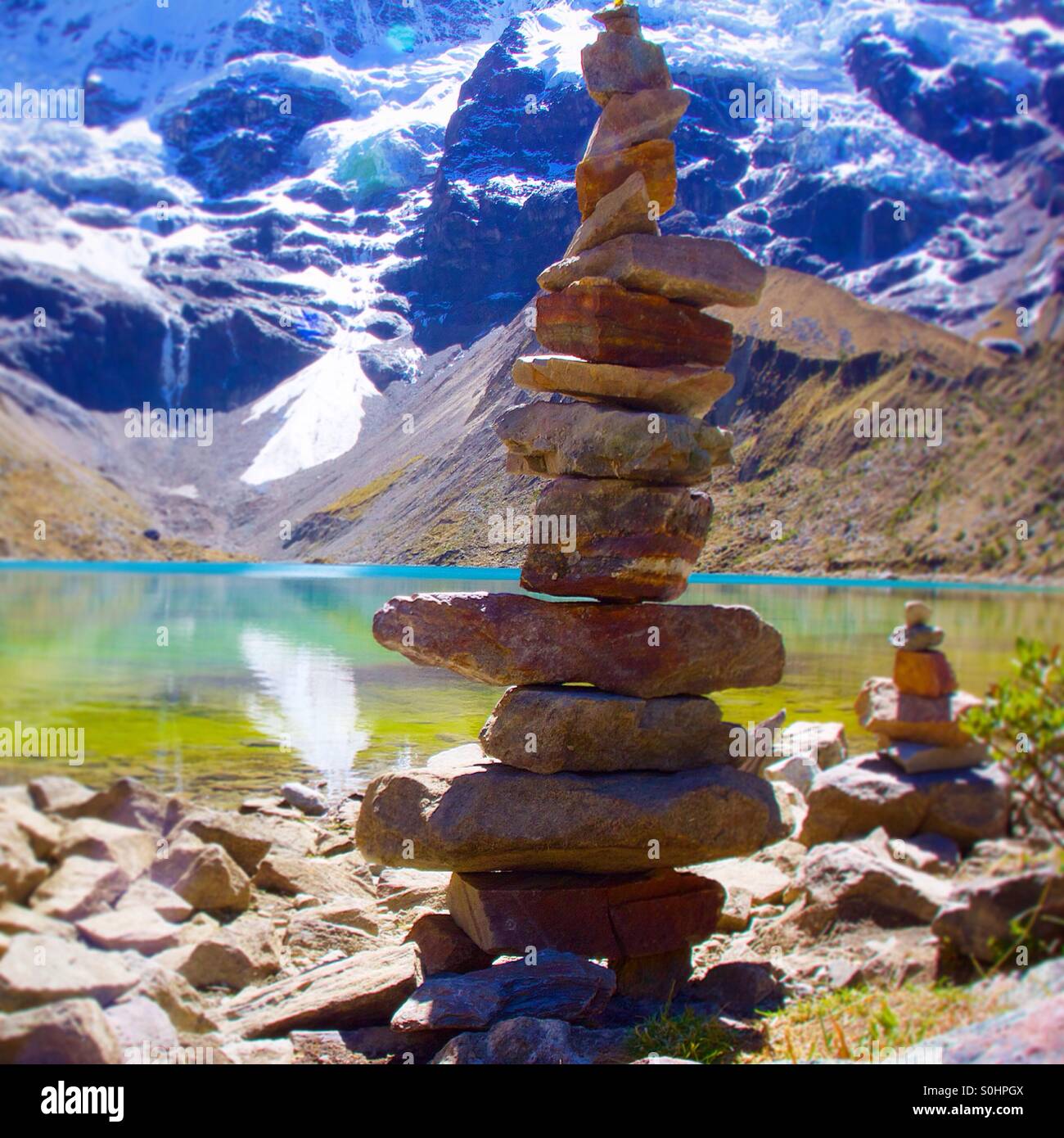 A carefully stacked rock tower is placed with this high elevation, glacier fed lake, reflection blue skies and green algae. Stock Photo
