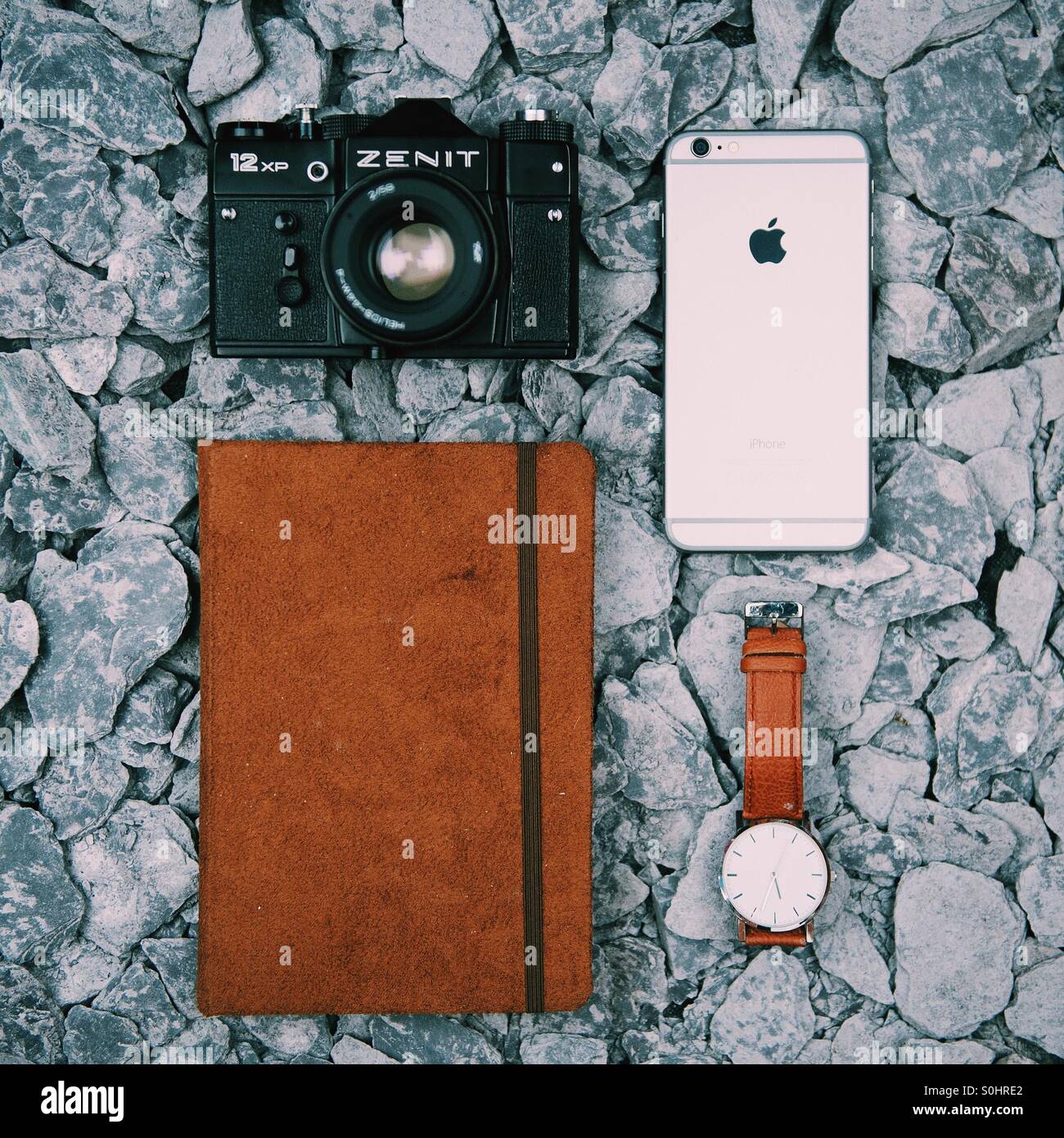 A Zenit 12xp Film Camera along side a brown leather watch, brown notebook and iPhone 6 plus with slate as the background Stock Photo