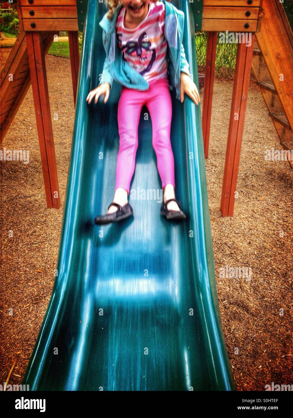 Young girl sliding down slide in playground Stock Photo