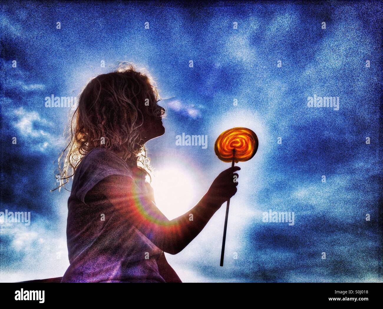 Young girl holding yellow swirly candy lolly backlit by sun Stock Photo