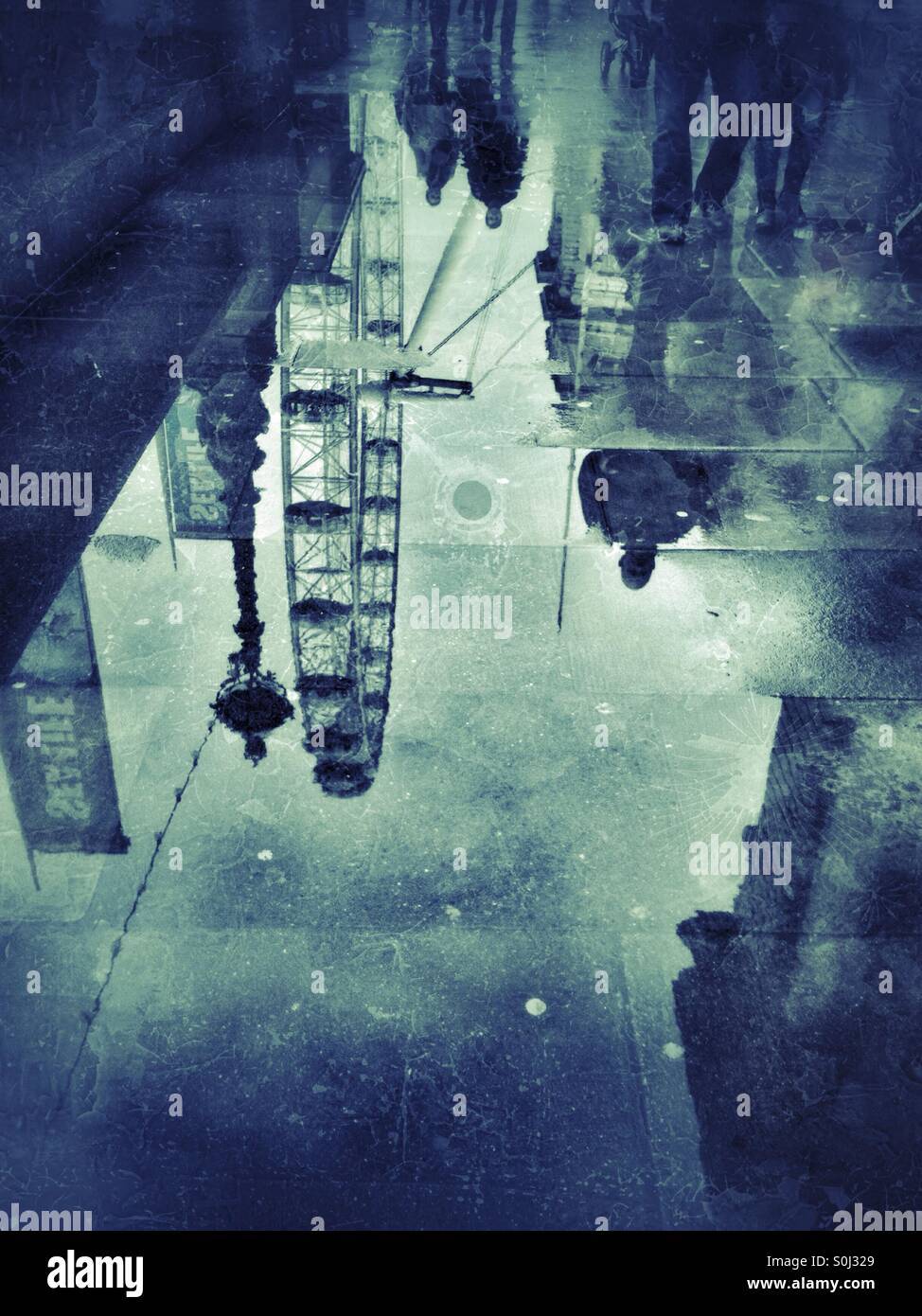 A rainy day in London Town - the reflection of passers by and the London Eye big wheel appear in a puddle. - Smartphone Captured Stock Image
