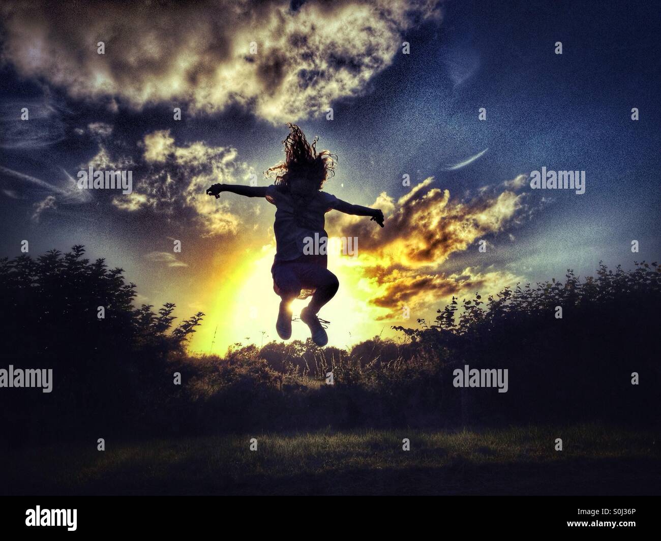 Young girl jumping backlit by late evening sun Stock Photo