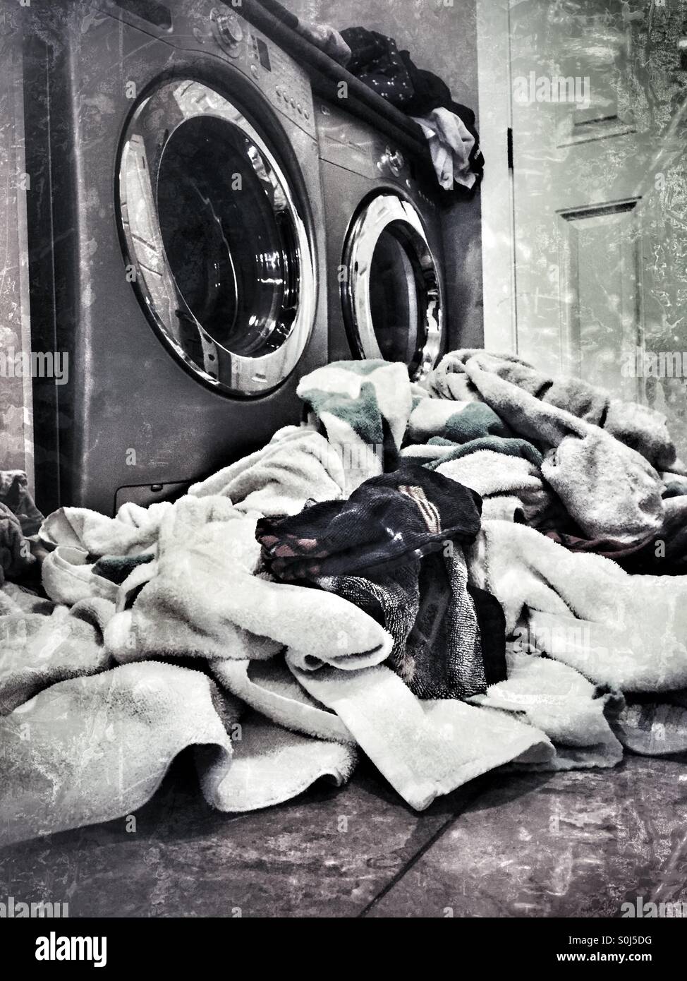 A daunting scene of piled up laundry in front of washing machine and dryer duo. - Smartphone Captured Stock Image