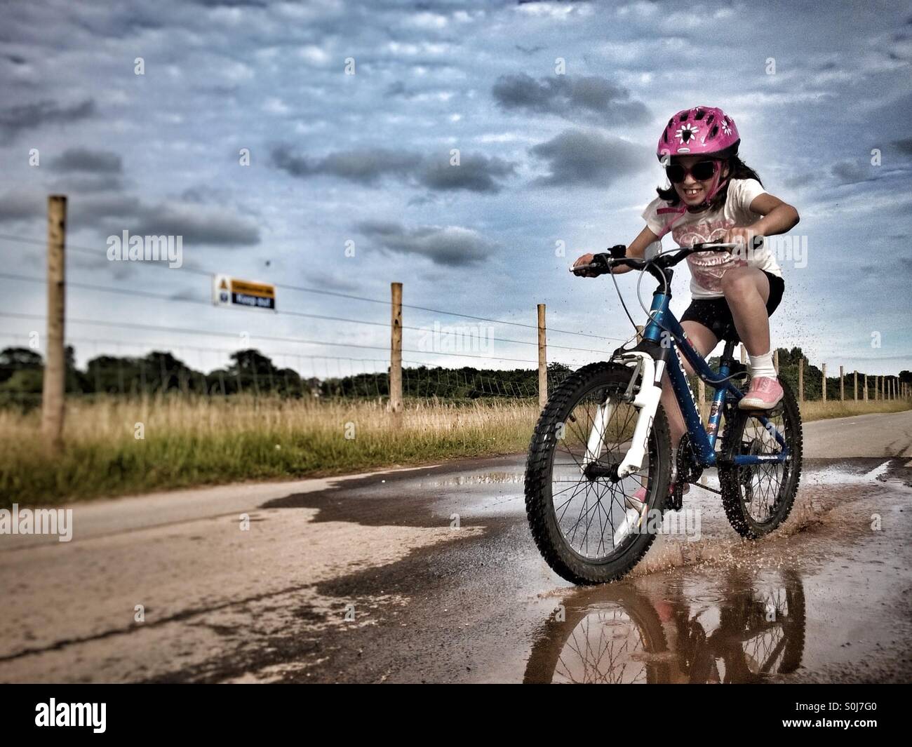 Girl having fun riding bicycle through a puddle. - Smartphone Captured Stock Image