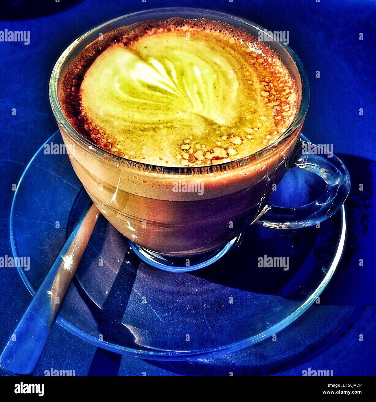 Dramatic colours of flat white coffee in glass cup with saucer and spoon - Smartphone Captured Stock Image