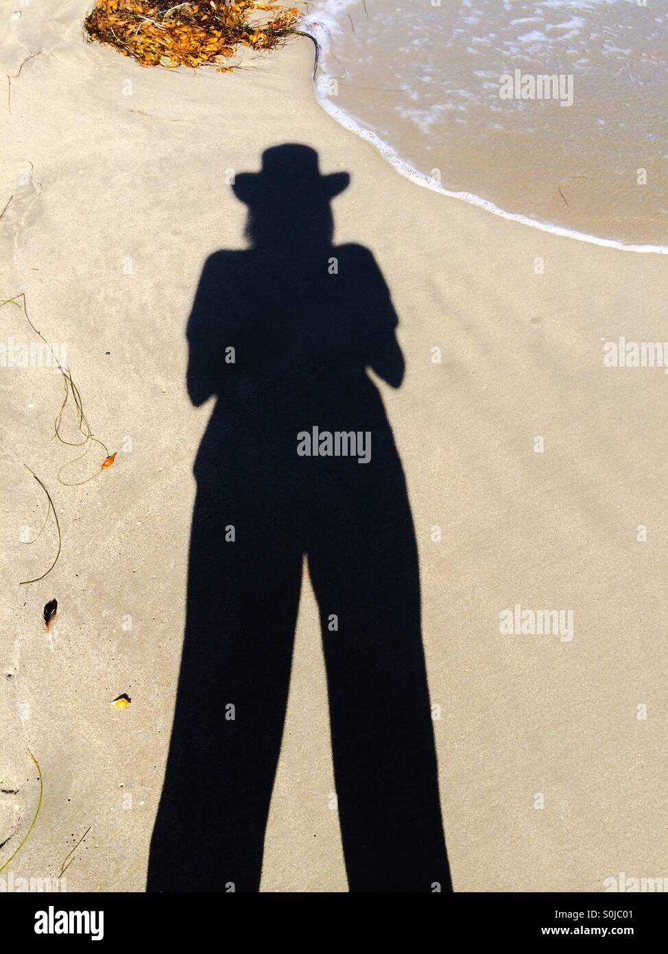 Shadow of a tall female wearing a hat at the beach Stock Photo