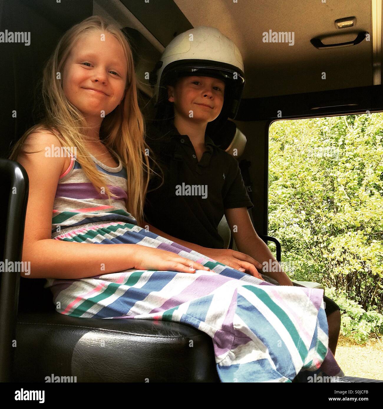 Two relieved and happy kids are sitting in a fire truck after fire in their yard was put out . Stock Photo