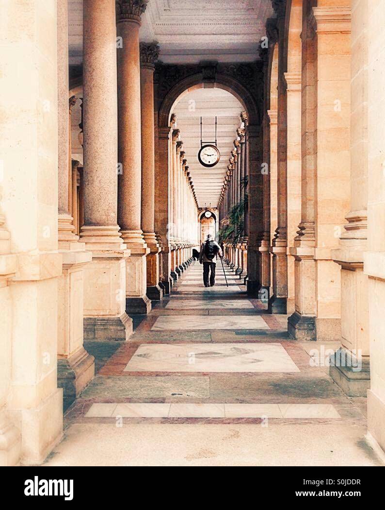 old man with crutch walking down the pillars alley in karlovy vary Stock Photo