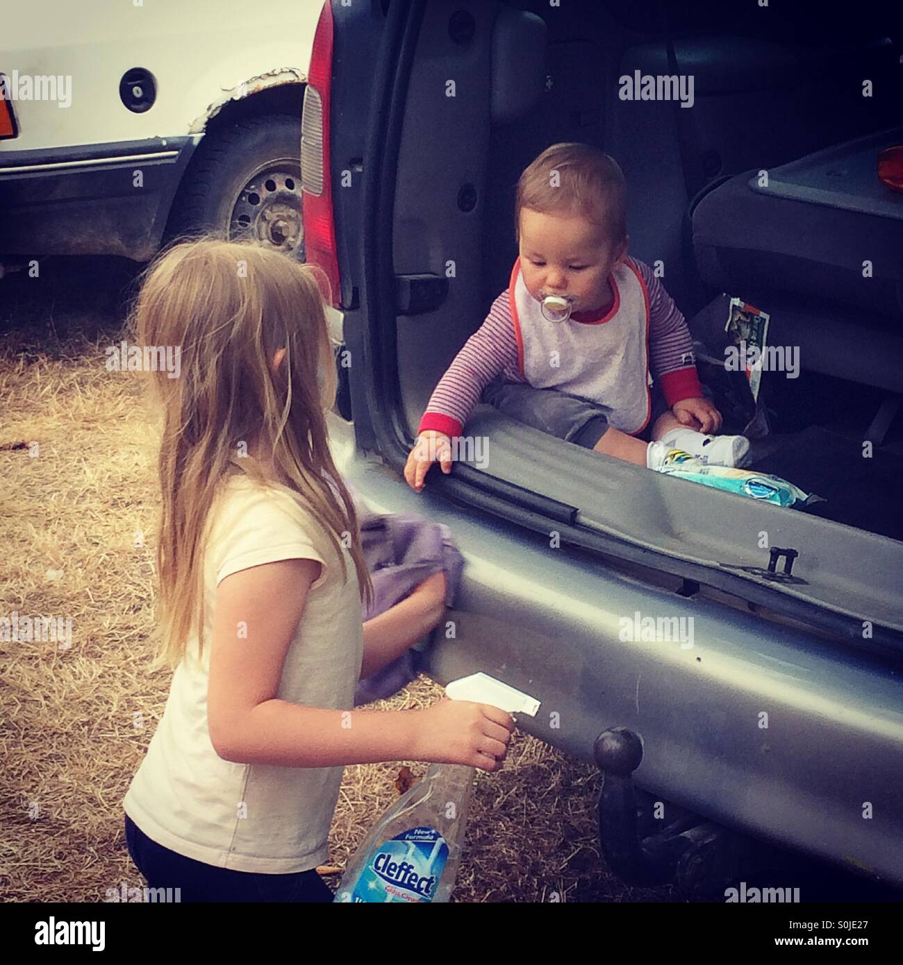 Baby Boy Sitting In The Trunk Of A Van Is Pointing At A Cloth Held By His Sister Who Is Washing The Car Stock Photo Alamy