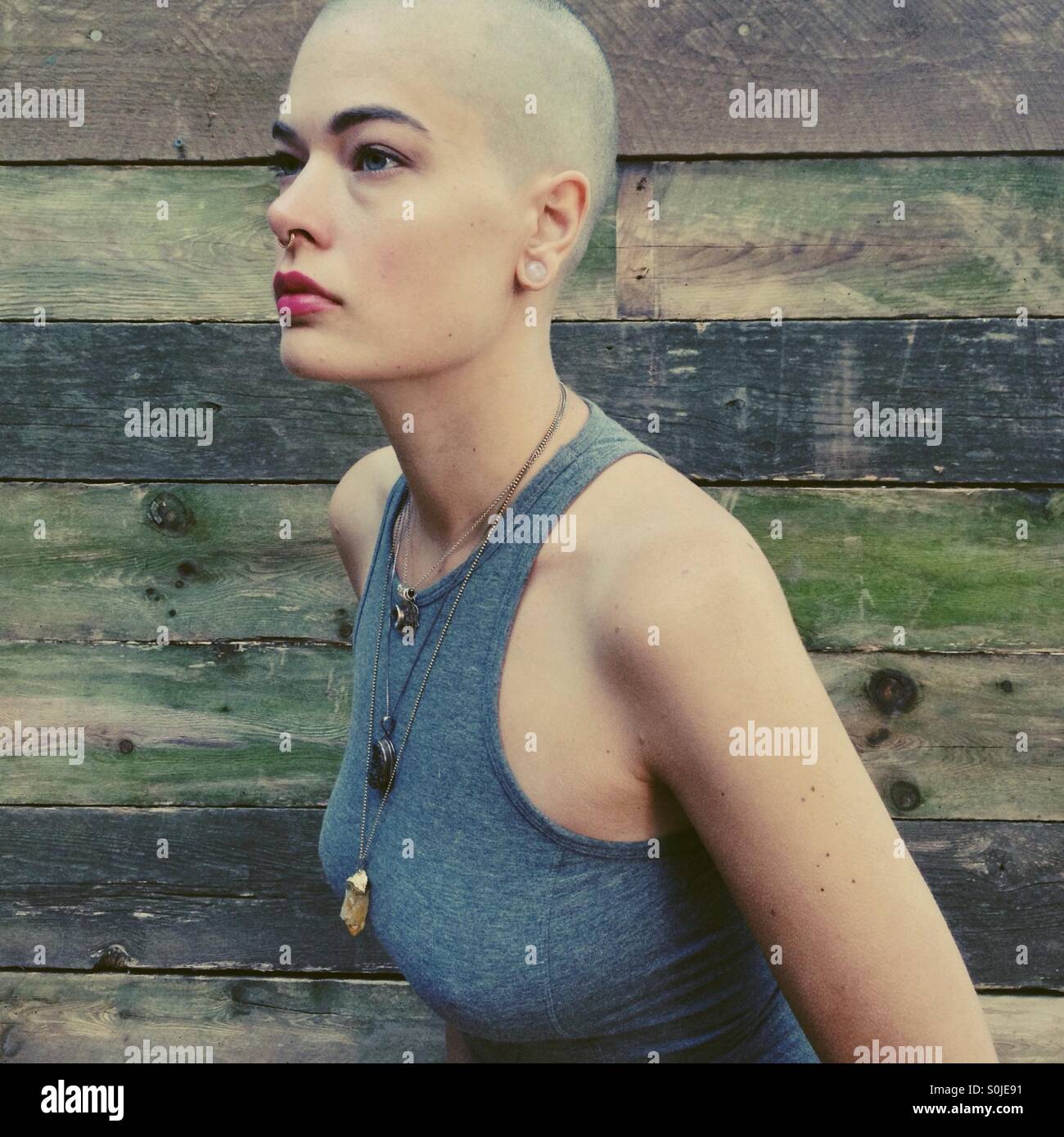 Bald woman with shaved head posing in front of wood background. Stock Photo