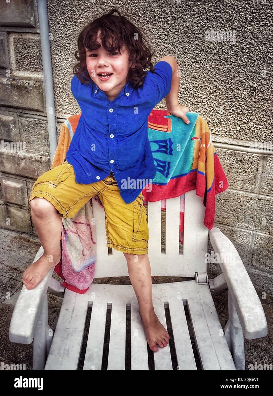 Four year old boy standing on patio chair Stock Photo