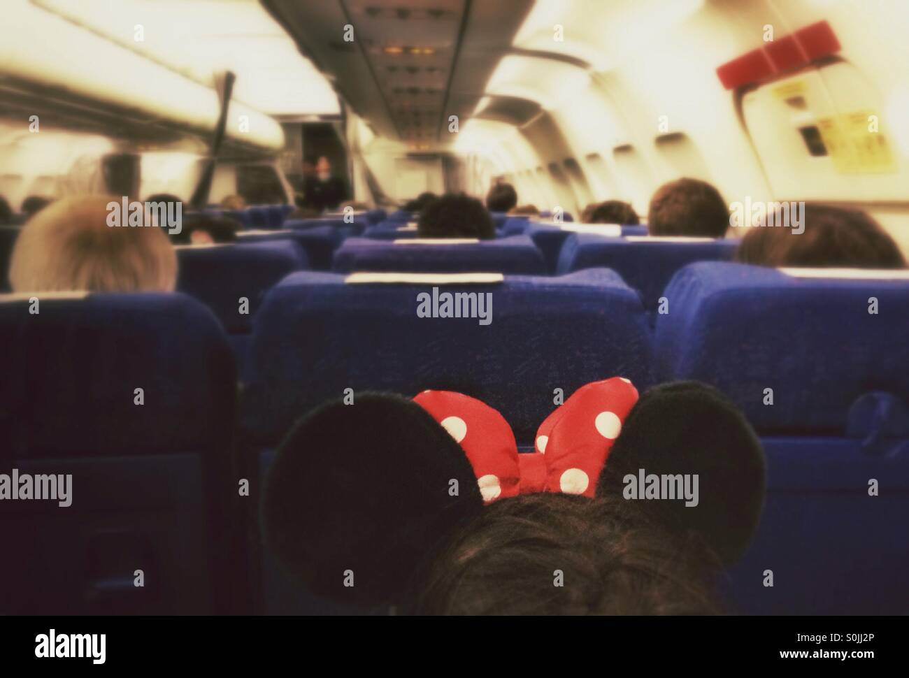 Inside of an airplane with passengers. Girl with Minnie Mouse ears headband in foreground. - Smartphone Captured Stock Image