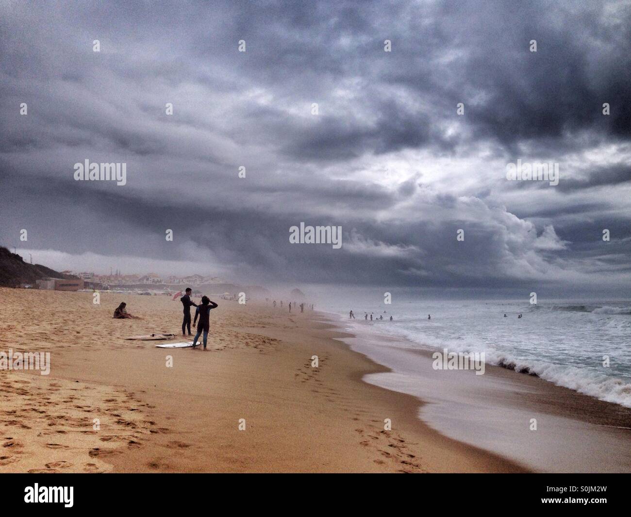 People surfing under a storm in the Atlantic Ocean, west coast of Portugal, with huge dark and gray clouds in the sky - Smartphone Captured Stock Image