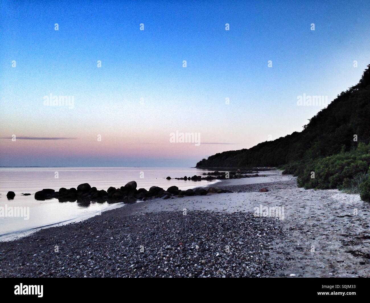 Desert and empty beach at sunset, in the east coast of Denmark, in Aarhus, Jutland. The forest on the right and the sunset orange colors over the sea in the left - Smartphone Captured Stock Image