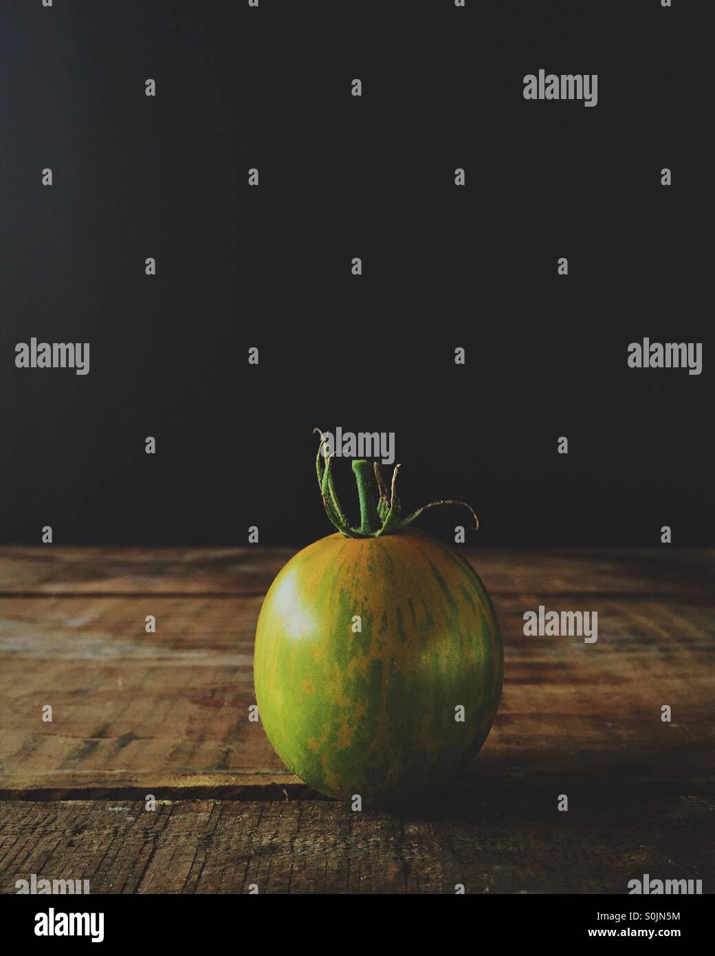 Organic green zebra tomato on a wood box with black background - Smartphone Captured Stock Image