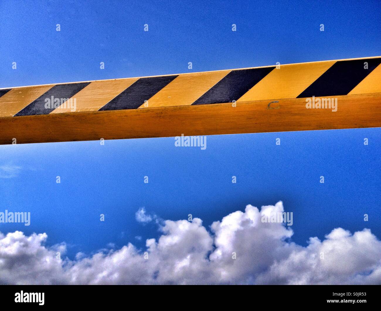 Yellow an black height warning bar contrasted against a blue sky with fluffy clouds - Smartphone Captured Stock Image