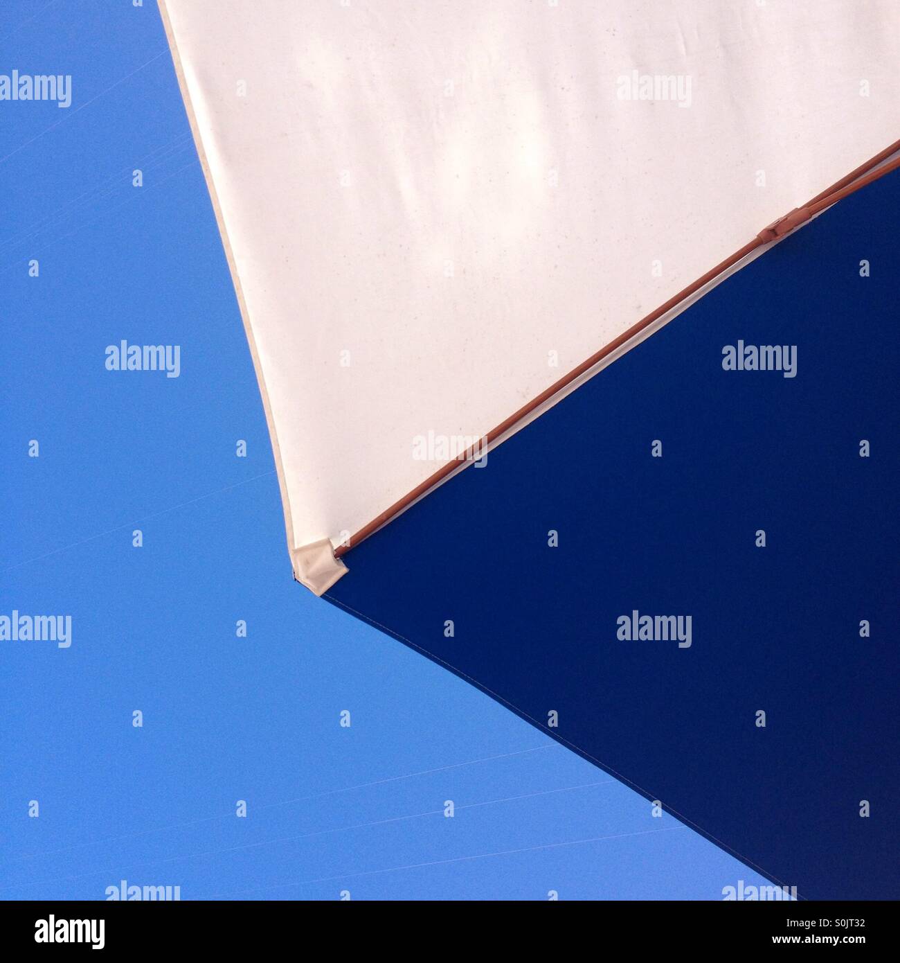 Underside closeup of blue and white sun umbrella against a blu sky. - Smartphone Captured Stock Image