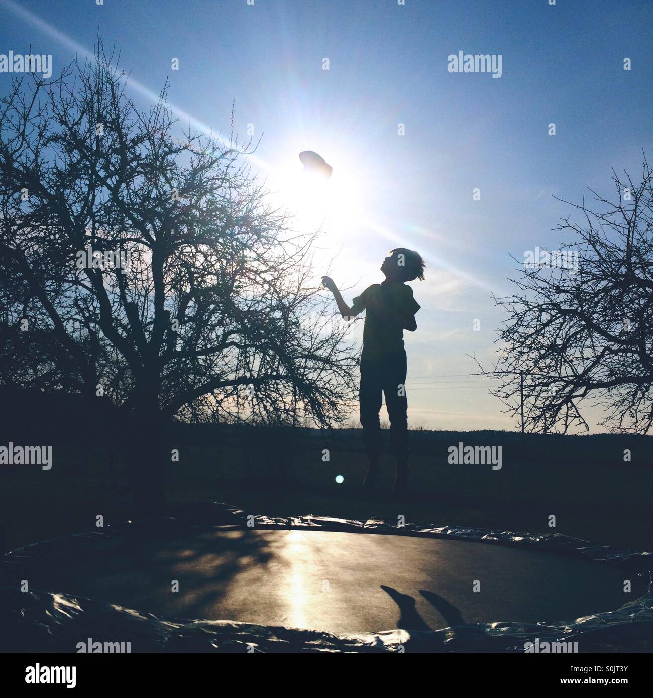 Silhouette of boy jumping on a trampoline, throwing his cap in the air Stock Photo