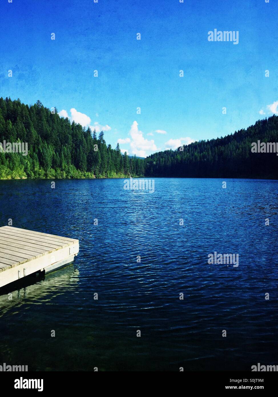 Blue mountain lake surrounded by trees under a blue sky. - Smartphone Captured Stock Image
