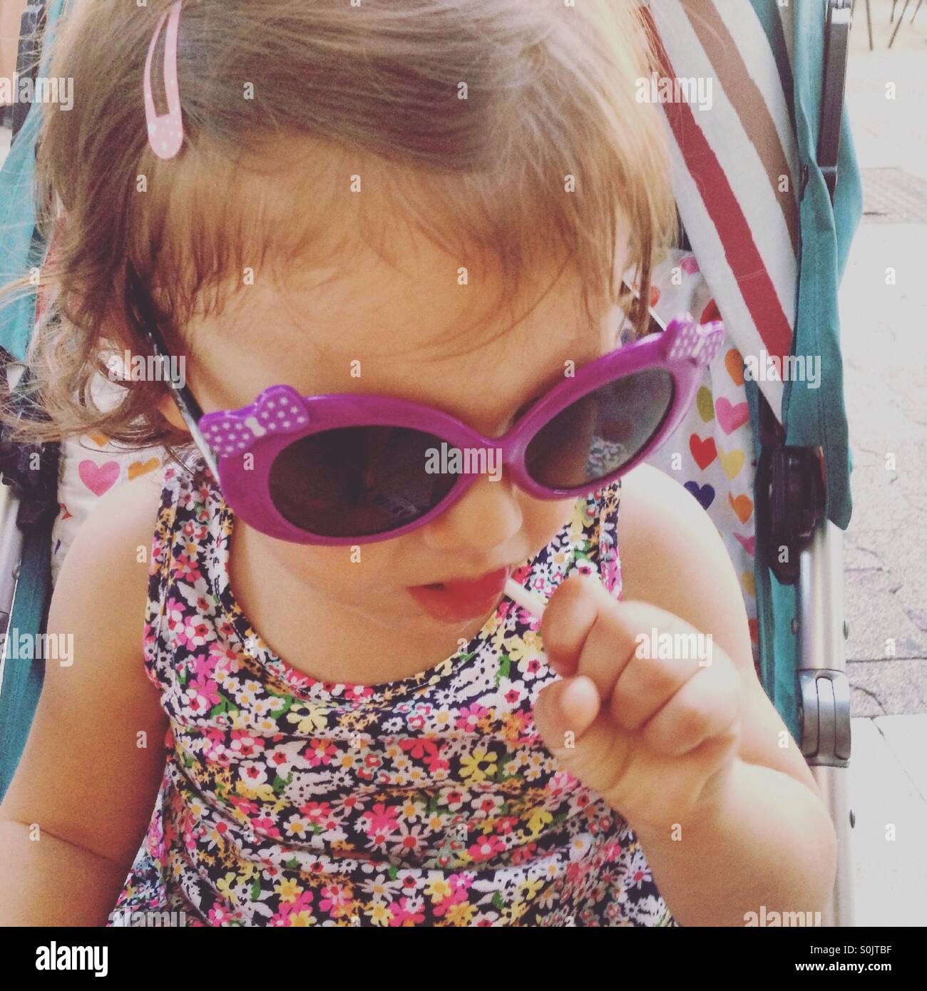 Baby girl with sunglasses and lollipop in mouth Stock Photo