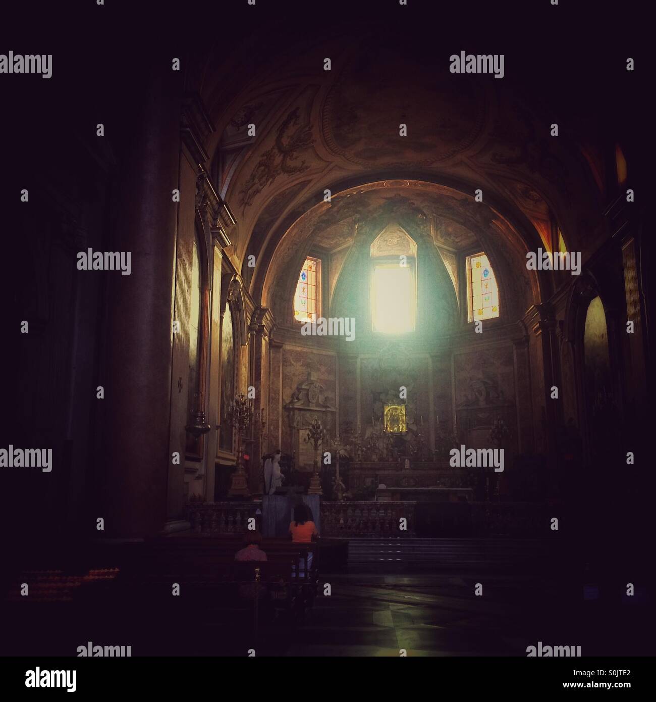 Light shining through a high window in Santa Maria Degli Angeli church Rome while 2 people pray - Smartphone Captured Stock Image