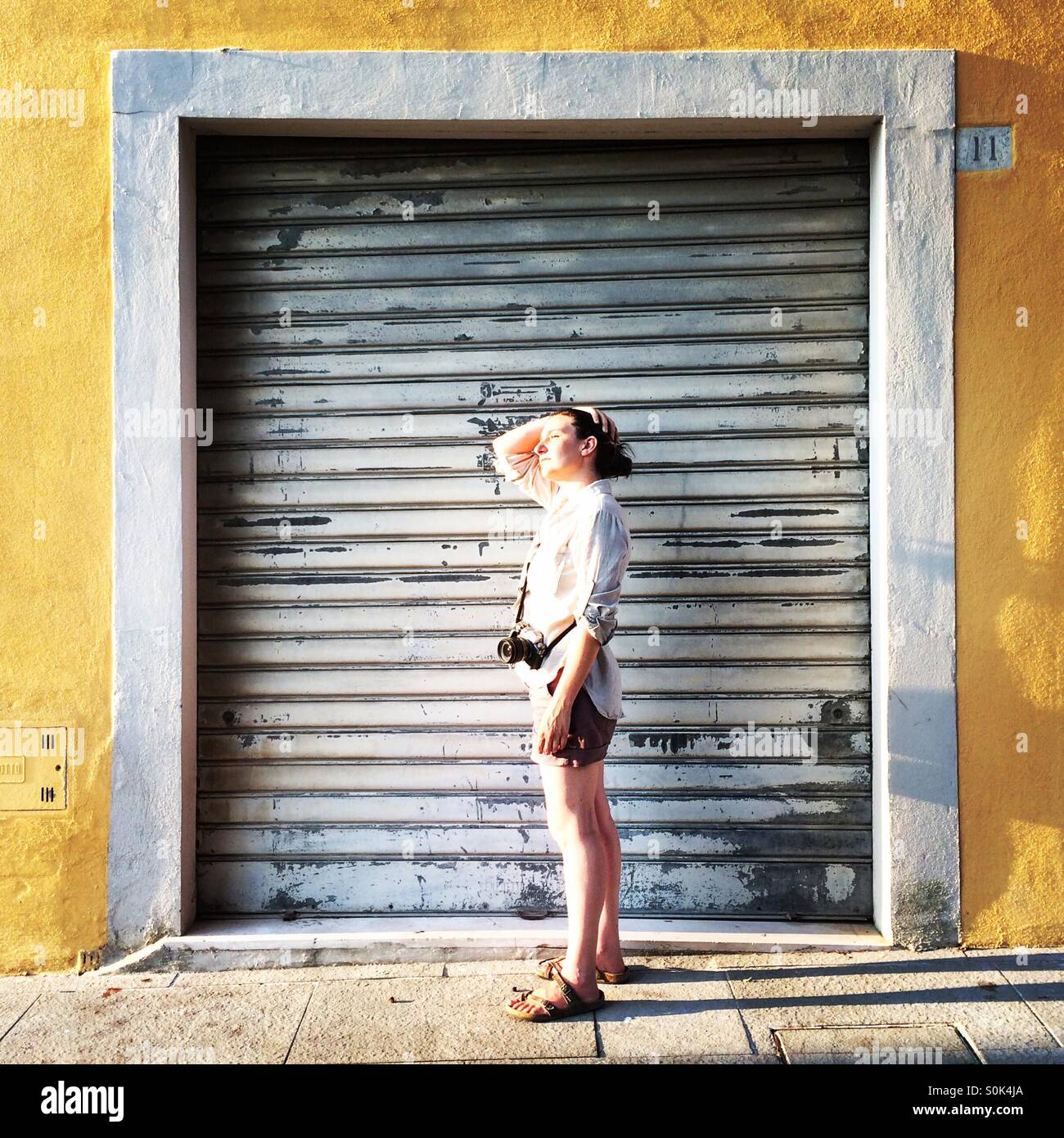 A female photographer with her camera in Arezzo, Tuscany, framed by a shuttered doorway. - Smartphone Captured Stock Image