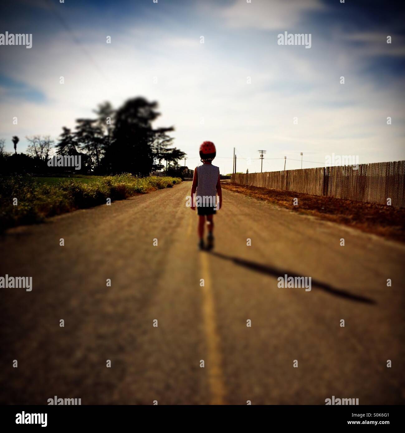 A 7 year old boy walks down the middle of a country road wearing his bicycle helmet. Stock Photo