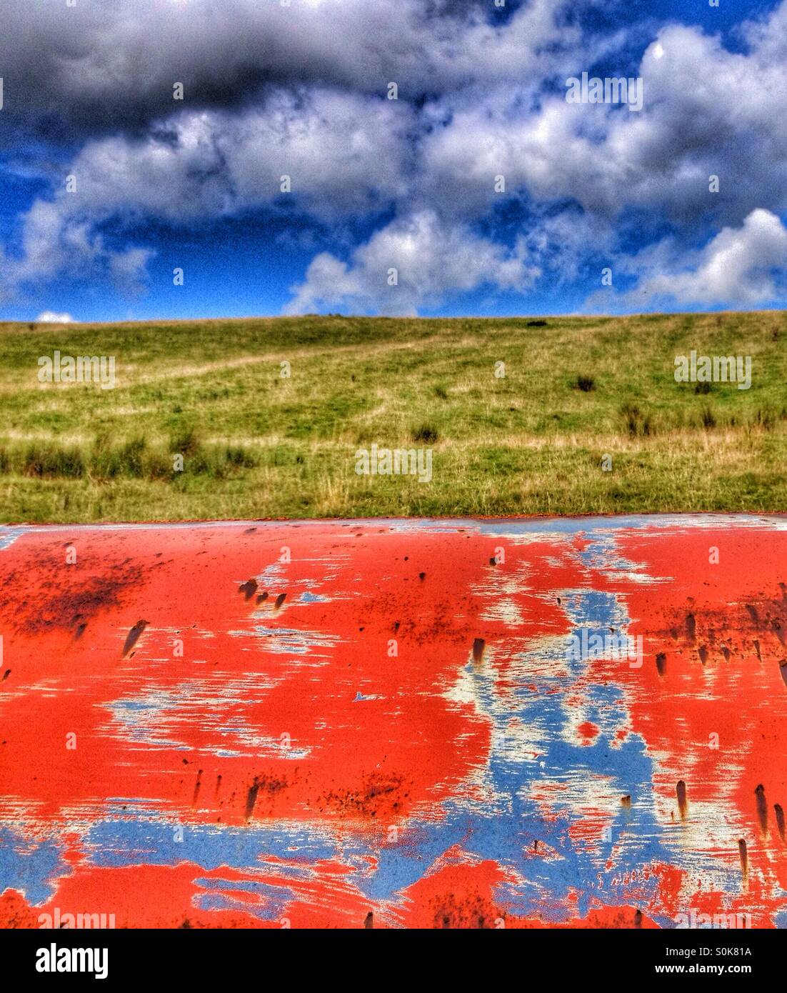 Old paint textures against green grass and cloudy blue sky - Smartphone Captured Stock Image
