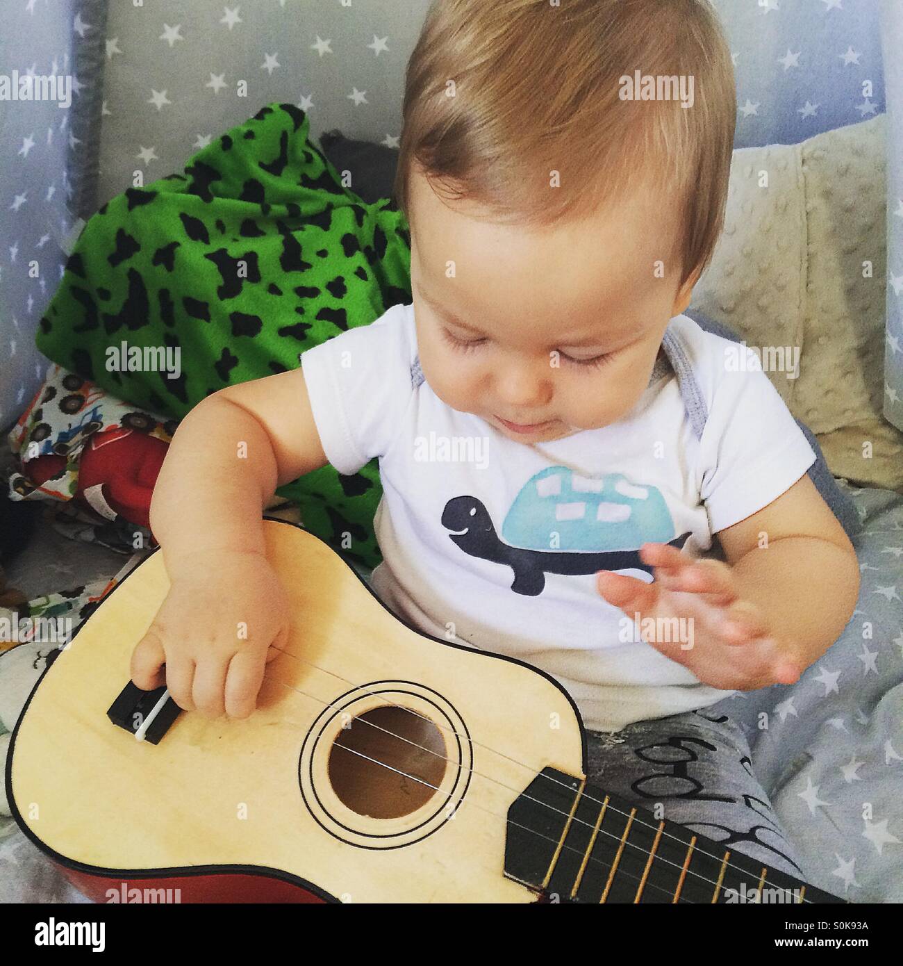 Baby boy sitting in his teepee surrounded by toys  concentrating and playing guitar Stock Photo