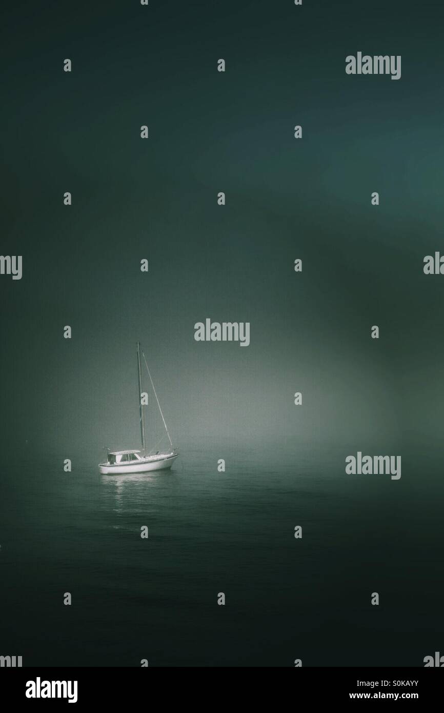 A single sail boat floating alone on a misty ocean. - Smartphone Captured Stock Image