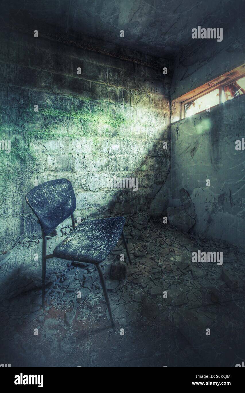 An old chair sits in a small derelict room with a shaft of light shining from a small window. - Smartphone Captured Stock Image