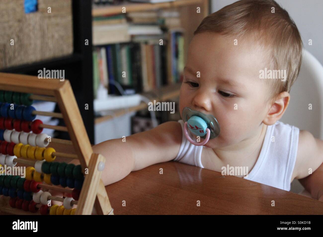9 months old baby boy with a pacifier in his mouth , is touching the abacus Stock Photo