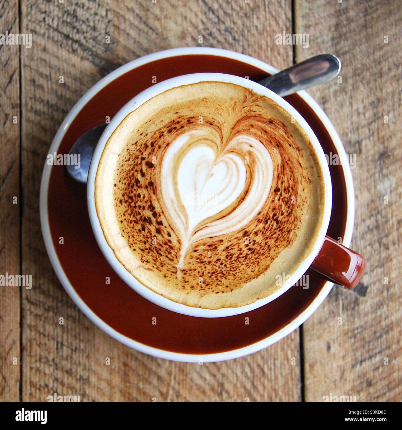 A coffee cup with a heart shaped finish sat on a wooden table - Smartphone Captured Stock Image