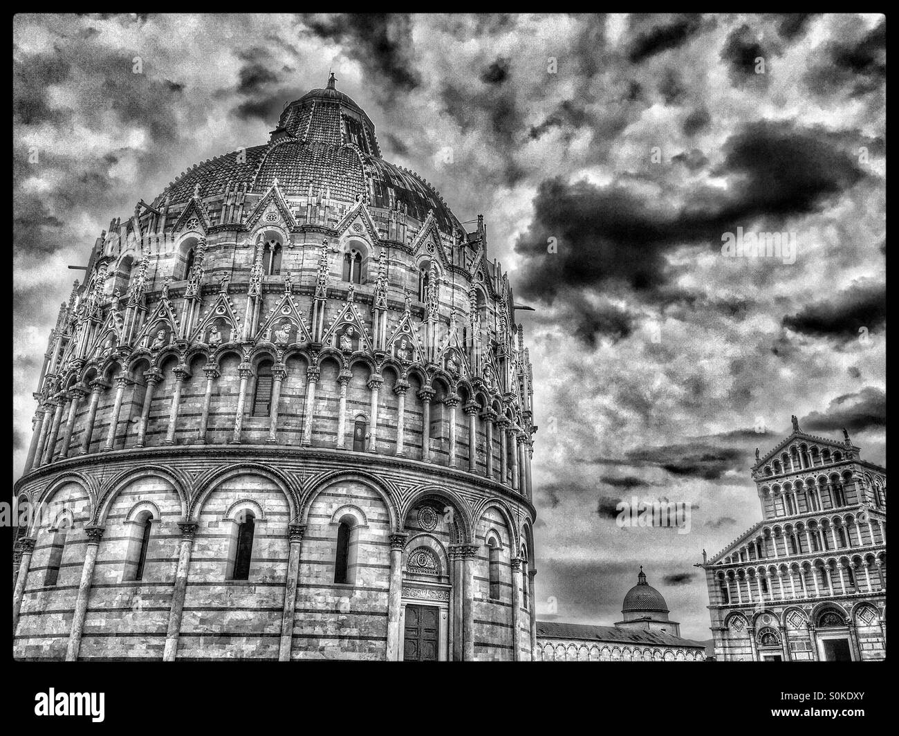 A Monochrome, Storm Clouds View of The Field of Miracles in Pisa, Tuscany, Italy. On the left is the Baptistery, bottom centre the Camposanto & to the right, The Duomo. Photo Credit-COLIN HOSKINS. - Smartphone Captured Stock Image