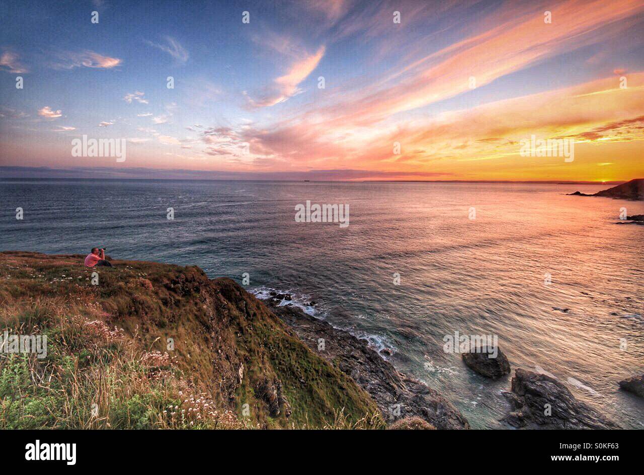 A photographer watching a sunset over a calm Ocean from a cliff edge - Smartphone Captured Stock Image