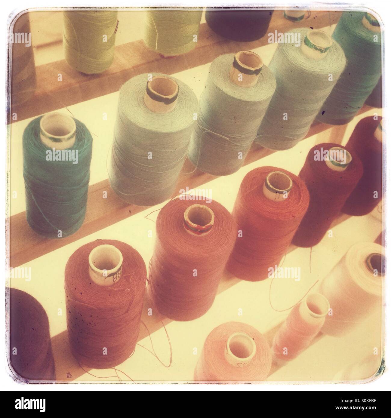 Colorful assortment of sewing thread spools organized by shade in a bright workspace - Smartphone Captured Stock Image