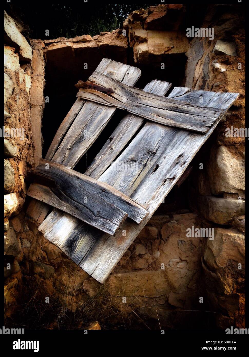 Broken wooden door on a stone built cistern, Catalonia, Spain. - Smartphone Captured Stock Image