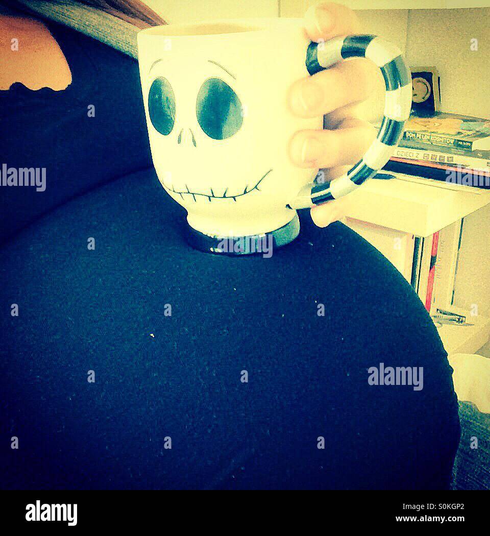 Coffee mug being held on a woman's very pregnant belly covered with a black shirt Stock Photo