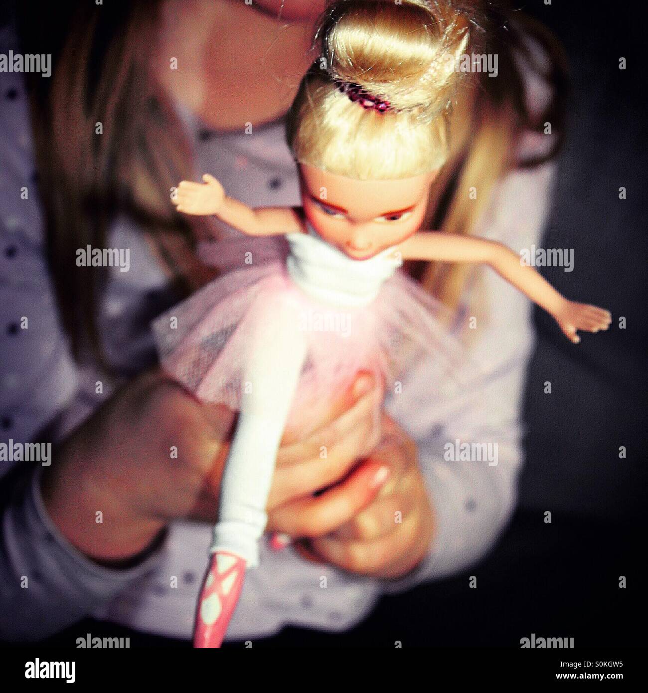 A girl is playing affectionately with her ballerina doll , holding her by one led, pretending to dance with her Stock Photo