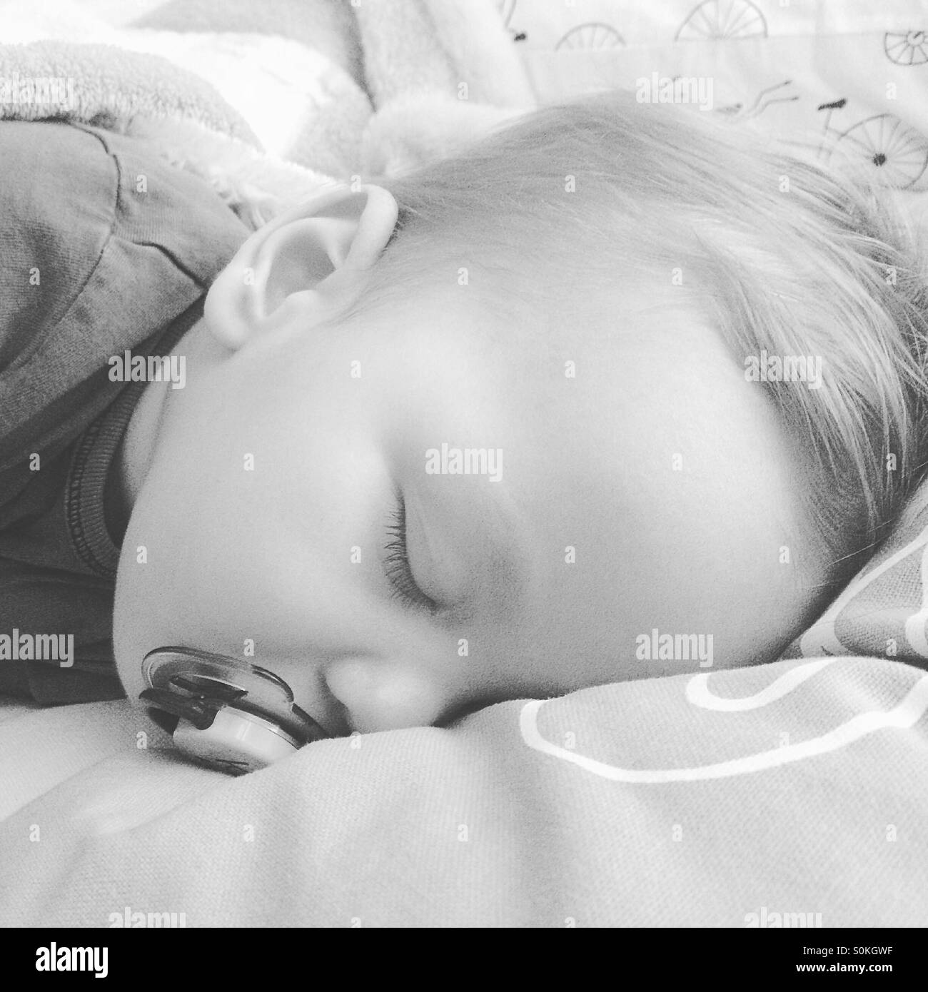 9 month old baby boy , teething, feverish is taking a nap with his pacifier on his parents bed Stock Photo