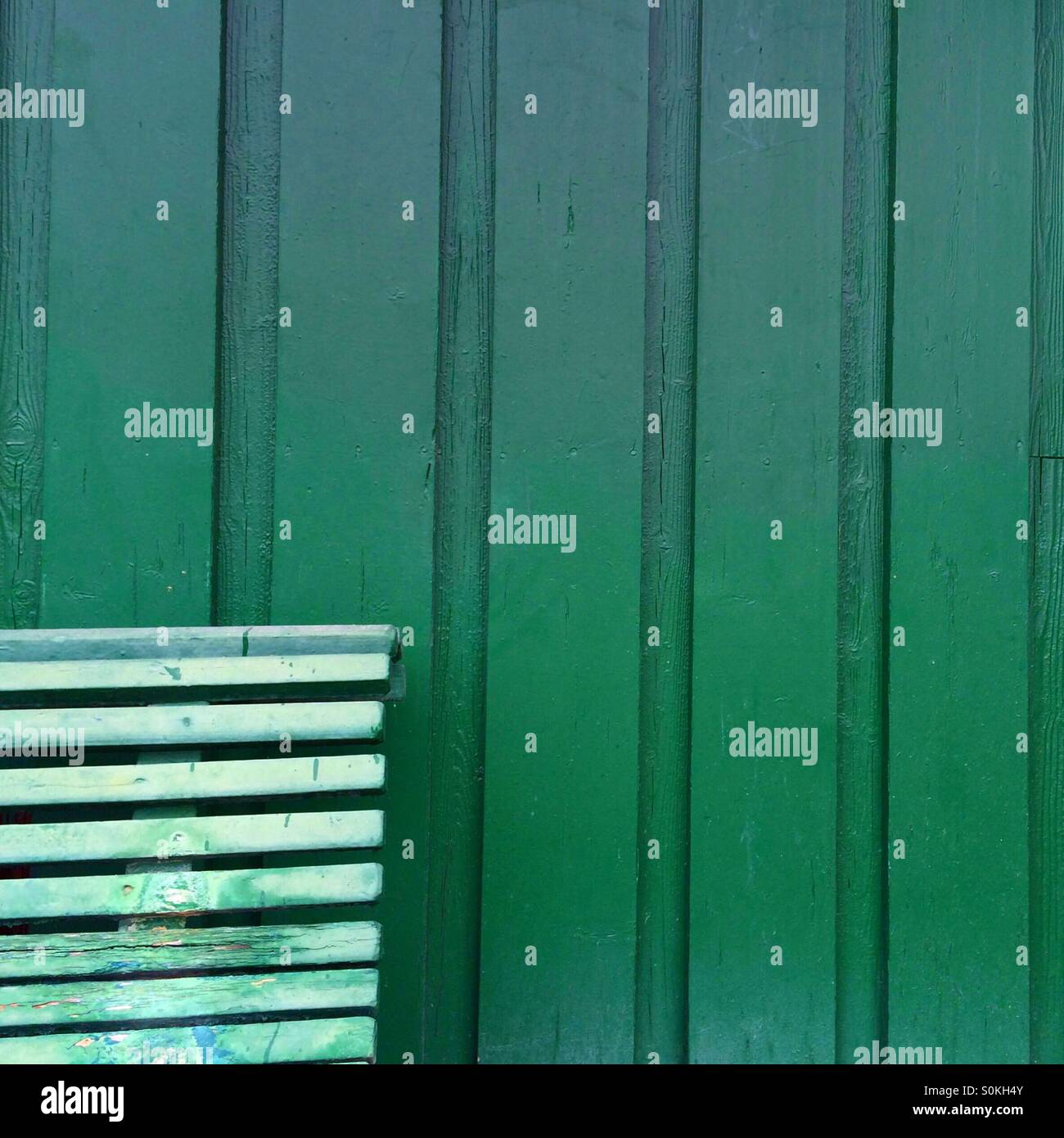 Part of a green wood bench in front of a green door - Smartphone Captured Stock Image