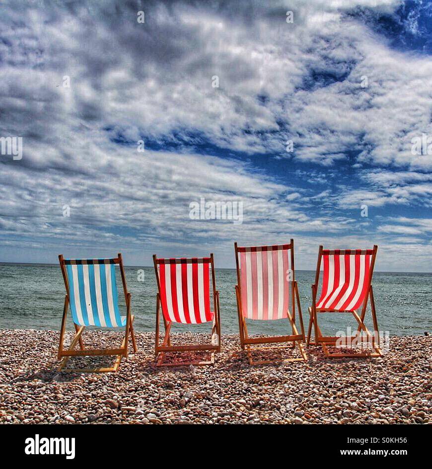 Four empty deckchairs sitting on a deserted pebble beach. - Smartphone Captured Stock Image